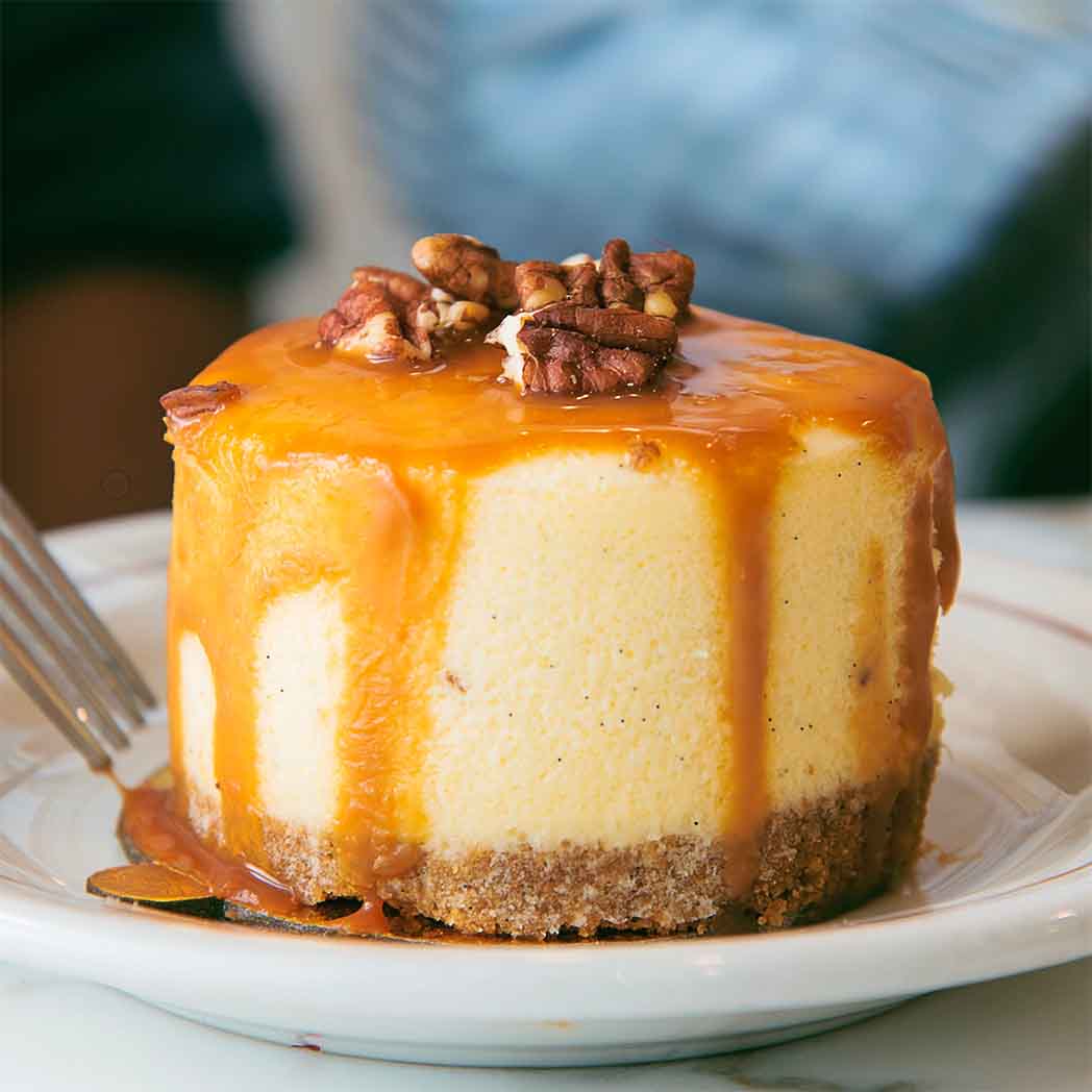 a desert on a white place with medium brown caramel pouring over the sides and walnuts on top