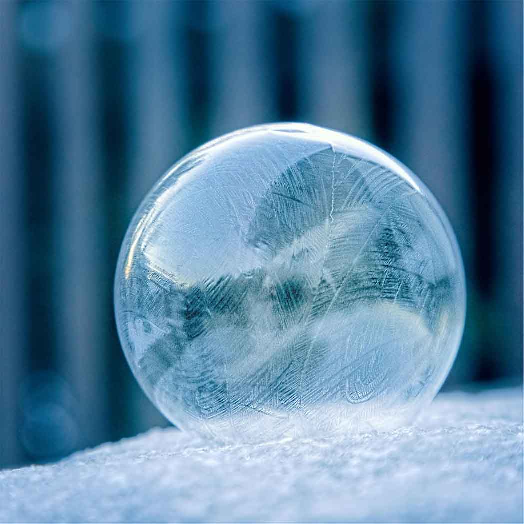 bubble sitting on snow beginning to get ice lines, all in shades of blue